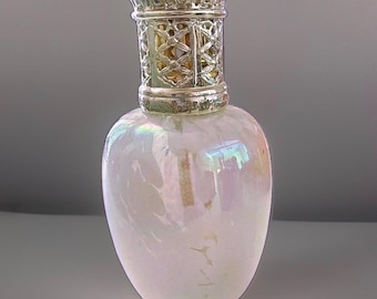 May include: A pearlescent glass fragrance lamp with an iridescent finish that reflects light in soft pink and blue tones. The vessel features a rounded body and is topped with a decorative, perforated silver-colored metal crown cap.