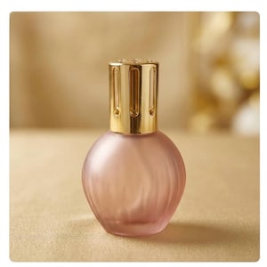 May include: A spherical fragrance lamp with a frosted, pale pink glass base featuring vertical ribbed detailing. The top of the lamp is fitted with a polished gold-tone metal crown cap that has vertical cutouts for ventilation and diffusion.