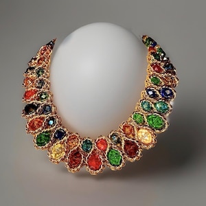 May include: A crescent-shaped statement necklace featuring a gold-toned twisted metal chain setting. The piece is adorned with numerous faceted, multi-coloured glass stones in shades of red, green, blue, and yellow, arranged in a dense, layered pattern.