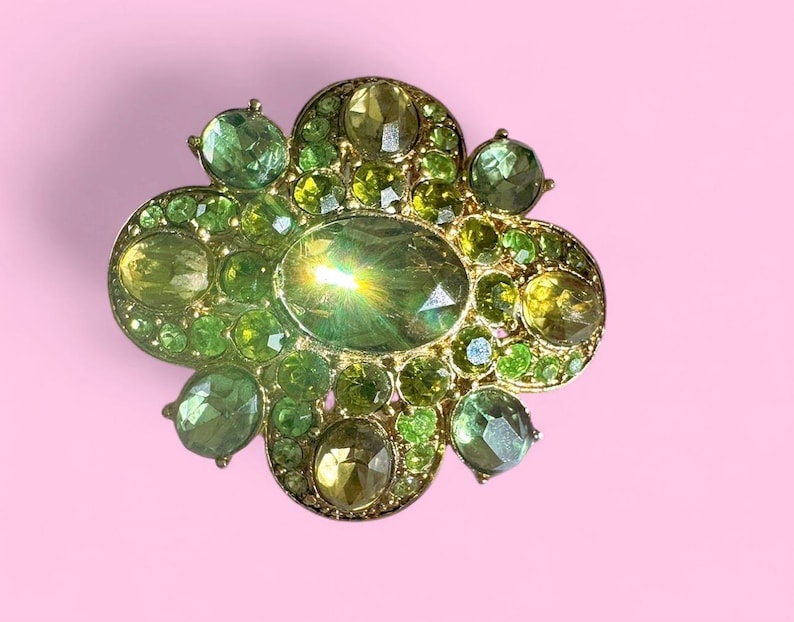 Peut inclure: Broche dor&eacute;e de forme florale orn&eacute;e d'un assortiment de pierres pr&eacute;cieuses vertes et jaunes. La broche pr&eacute;sente une pierre centrale ovale entour&eacute;e de petites pierres rondes et ovales de diff&eacute;rentes nuances de vert et de jaune.