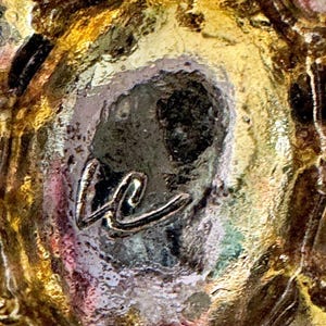 Peut inclure: Gros plan sur une surface textur&eacute;e multicolore avec des teintes dor&eacute;es, marron et violettes. Un monogramme stylis&eacute; "kc" de couleur argent&eacute;e est centr&eacute;, ajoutant une touche d'&eacute;l&eacute;gance au design abstrait.