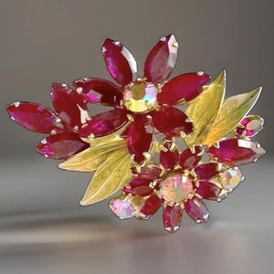 May include: A floral brooch featuring deep red marquise-cut crystals arranged in two flower clusters. The design includes gold-toned metal leaves and two central iridescent crystals that reflect light with a multi-colored shimmer effect.