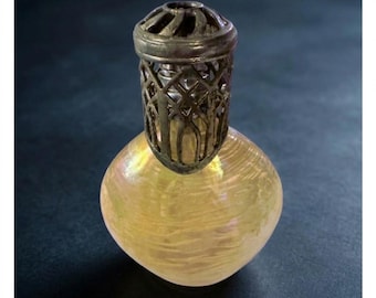 May include: A small, rounded glass fragrance lamp with a pale yellow, iridescent finish. The top features a decorative, dark metallic cage with an intricate, open-work lattice design that sits securely over the neck of the glass vessel.