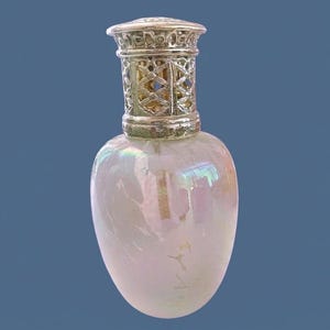 May include: A fragrance lamp with a pearlescent, iridescent glass body that displays soft pink and white swirls. The top features a decorative, perforated silver-toned metal crown with a lattice pattern, securely fitted to the neck of the vessel.