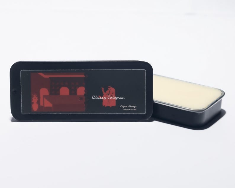 May include: A black rectangular tin with rounded corners, featuring a red graphic of a lounge scene and the text "Classy Colognes." Beside it, a matching open tin reveals a solid, light-colored cologne. The product is designed for men.