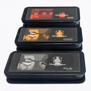 May include: Three black rectangular tins with transparent lids are stacked. Each tin features a different graphic illustration and the text "Classy Colognes." The top tin has a red bar scene, the middle tin has a brown bar scene, and the bottom tin has a gray bar scene.