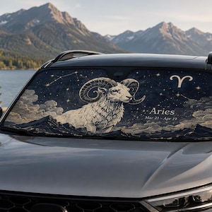 May include: A car windshield sun shade featuring a dark blue celestial background with a white ram illustration, the Aries zodiac symbol, the text Aries, and the dates Mar 21 - Apr 19. The design includes golden stars, constellations, and clouds.