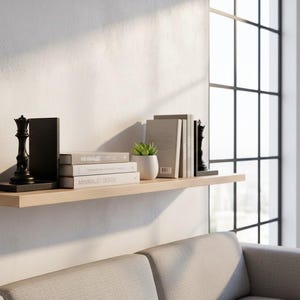 May include: A wooden shelf displays a black chess piece, books, and a small potted plant. The books are stacked and labeled "Minimalist Design". The shelf is mounted on a white wall, with a window in the background.