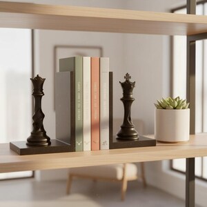 May include: A bookshelf with decorative items. Two black chess pieces, a queen and a king, flank a stack of books with various colored spines. A small potted succulent sits to the right. The shelf is made of light wood.