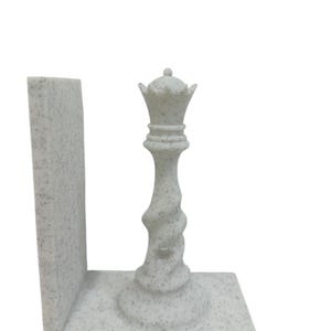 May include: A speckled white chess queen bookend. The queen piece is intricately detailed with a crown and a twisted stem. The bookend has a rectangular base and a vertical support, perfect for holding books.