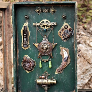 May include: A collection of steampunk-style metal embellishments mounted on a dark green wooden surface. The pieces include gears, a star-shaped medallion with a lion's head, and various decorative elements in bronze and copper tones.