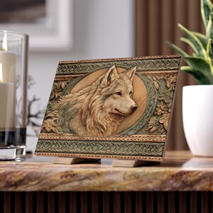 May include: A rectangular plaque featuring a detailed relief carving of a wolf head centered within an oval frame. The border displays intricate woven patterns and floral motifs in shades of brown, tan, and muted green, set on a small stand.
