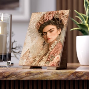 May include: A rectangular wooden tabletop display featuring a portrait of a person with dark hair adorned with pink flowers, wearing lace-trimmed clothing and dangling earrings. The background includes a butterfly illustration and ornate patterns.