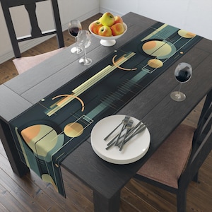 May include: A dark teal table runner with an abstract geometric design featuring circles and lines in shades of orange, yellow, and teal. The runner is placed on a dark wooden table set for a meal, with plates, silverware, and wine glasses.
