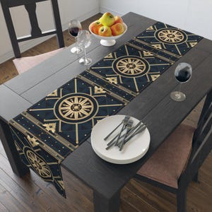 May include: A rectangular table runner featuring a dark navy blue background with a repeating gold geometric pattern of circular medallions and straight lines. The runner is laid across a dark wooden table with white plates and wine glasses.