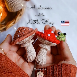 Puede incluir: Dos figuras de setas de ganchillo, una naranja con lunares blancos, la otra roja con lunares blancos, y una rana verde. La imagen incluye el texto "Mushroom and the Little Frog" y "E-BOOK".