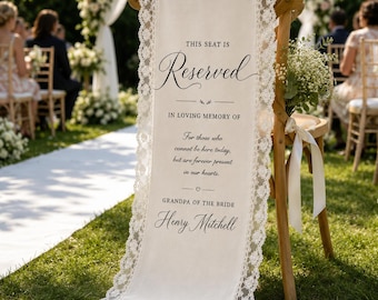 May include: A cream-colored fabric memorial sign draped over a wooden chair, featuring white lace trim. The text reads: This seat is Reserved in loving memory of For those who cannot be here today, but are forever present in our hearts. Grandpa of the bride Henry Mitchell.