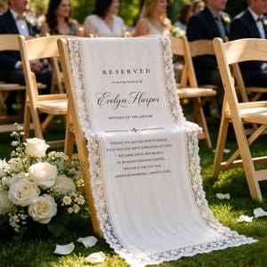 May include: A white fabric memorial sign draped over a wooden folding chair, featuring lace trim and black text that reads: RESERVED in loving memory of Evelyn Harper MOTHER OF THE GROOM, followed by a poem about love and spirit.