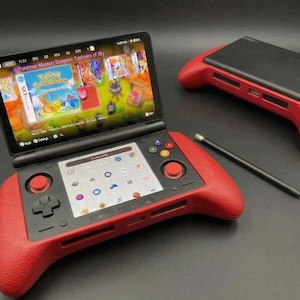 May include: A handheld gaming console with a red textured grip and a black screen displaying a game. A second console and a stylus are also present. The screen shows a game with colorful graphics. The console has buttons and a joystick.