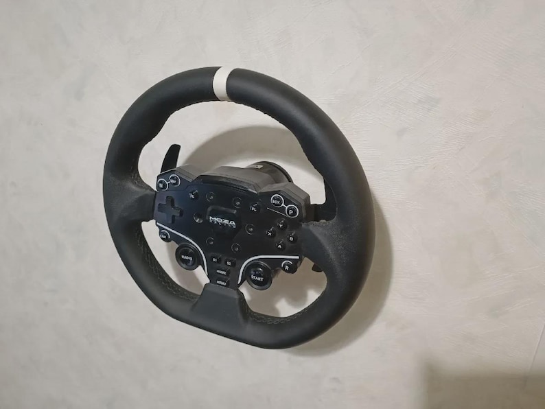 May include: Black racing wheel with a white stripe at the top. The wheel has a black control panel with buttons and the brand name "MOZA". The wheel is designed for use with a racing simulator.