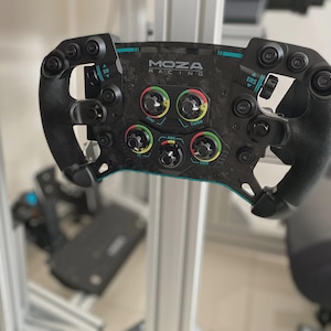 May include: A black and carbon fiber MOZA Racing steering wheel with multiple buttons and dials. The wheel has a curved design with a teal accent and the MOZA Racing logo. It is designed for sim racing.