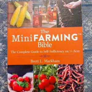 May include: The MiniFARMING Bible book cover. The cover features images of corn, jars of liquid, a hand sowing seeds, strawberries, tomatoes, and worms. The title is in large white letters on an orange background.