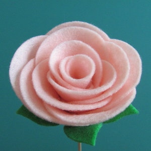 May include: A pink felt rose with green felt leaves. The rose is made of multiple layers of felt, creating a layered and textured look.