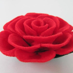 May include: A red felt rose with multiple layers of petals. The rose is a handmade craft item.