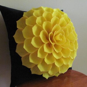 May include: A black pillow with a large yellow felt flower on the front. The flower is made of many individual petals.
