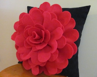 May include: A bright pink felt flower pillow on a black pillow cover. The flower is large and has many layers of petals.