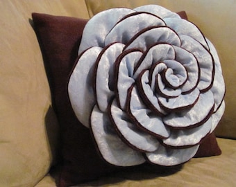 May include: A decorative throw pillow with a large, light blue velvet rose on a brown velvet background.