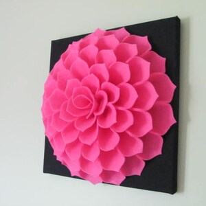 May include: A large pink felt flower on a black canvas. The flower is made up of many individual petals.