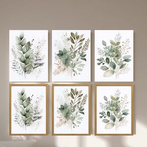 Könnte beinhalten: Sechs gerahmte botanische Kunstdrucke. Jeder Druck zeigt Aquarellillustrationen von grünen und beigen Blättern und Laub. Die Rahmen sind goldfarben und die Drucke werden an einer neutralfarbenen Wand über einem Tagesbett und einem Stuhl ausgestellt.