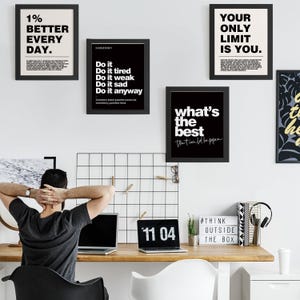 May include: A workspace featuring framed motivational posters with black frames and white text. The posters display phrases like "1% Better Every Day" and "Your Only Limit Is You." A laptop shows the time "11 04."