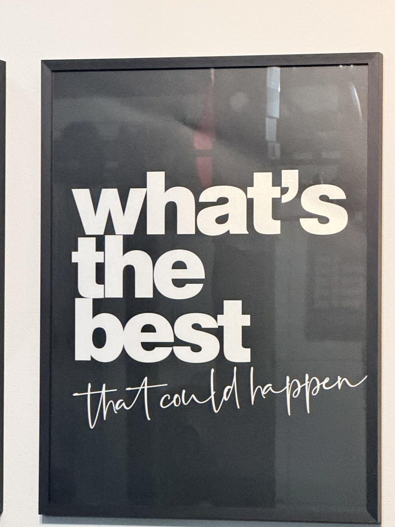 May include: Black framed print with white text that reads "what's the best that could happen" in a mix of bold and script fonts. The print is mounted on a white wall.