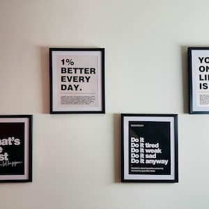 May include: Five framed motivational posters with black frames and white backgrounds. The posters display text such as "1% BETTER EVERY DAY" and "YOUR ONLY LIMIT IS YOU." The posters are mounted on a white wall.