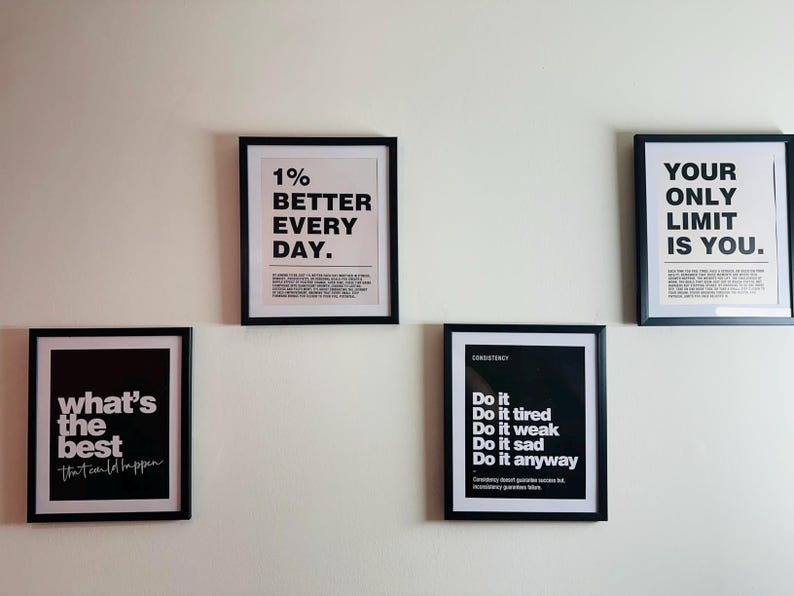 May include: Five framed motivational posters with black frames and white backgrounds. The posters display text such as "1% BETTER EVERY DAY" and "YOUR ONLY LIMIT IS YOU." The posters are mounted on a white wall.