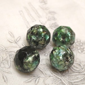 May include: Four faceted glass beads with a black and green iridescent finish. The beads have a speckled appearance and are arranged on a white surface.