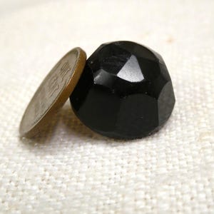 May include: A faceted, black bead with a coin next to it. The bead has a geometric design with multiple flat surfaces. The coin is a penny, showing the profile of Abraham Lincoln. The bead is approximately 0.75 inches in diameter.