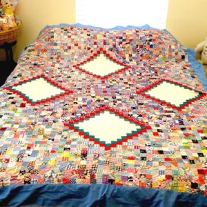 May include: A patchwork quilt featuring a multitude of small, multi-colored fabric squares in various patterns. The design includes four large, central white diamond shapes bordered by red and green square segments, all set against a blue base.