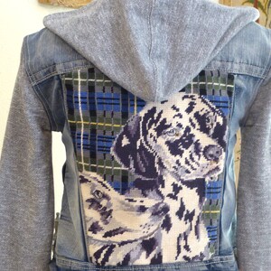 May include: A blue denim jacket with a gray hooded sweatshirt attached. The back of the jacket features a plaid fabric patch with a cross-stitch image of a Dalmatian dog.