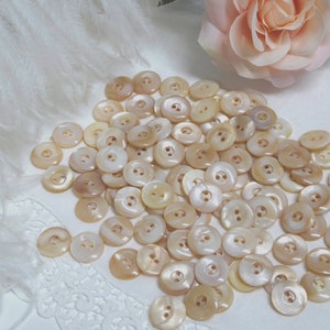 May include: A large pile of white and cream colored mother of pearl buttons. The buttons are round and have two holes.