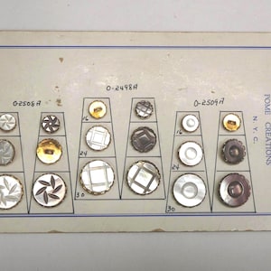 May include: A vintage display card featuring an assortment of decorative buttons in various sizes and designs. The buttons include gold, silver, and mother-of-pearl finishes. The card is labeled "POME CREATIONS N.Y.C."