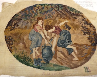May include: A needlepoint tapestry featuring an oval scene of two figures by a stream, one holding a dark blue pitcher. The figures wear muted blue and red clothing. The background depicts trees and foliage in shades of brown and green. Text reads A la source.