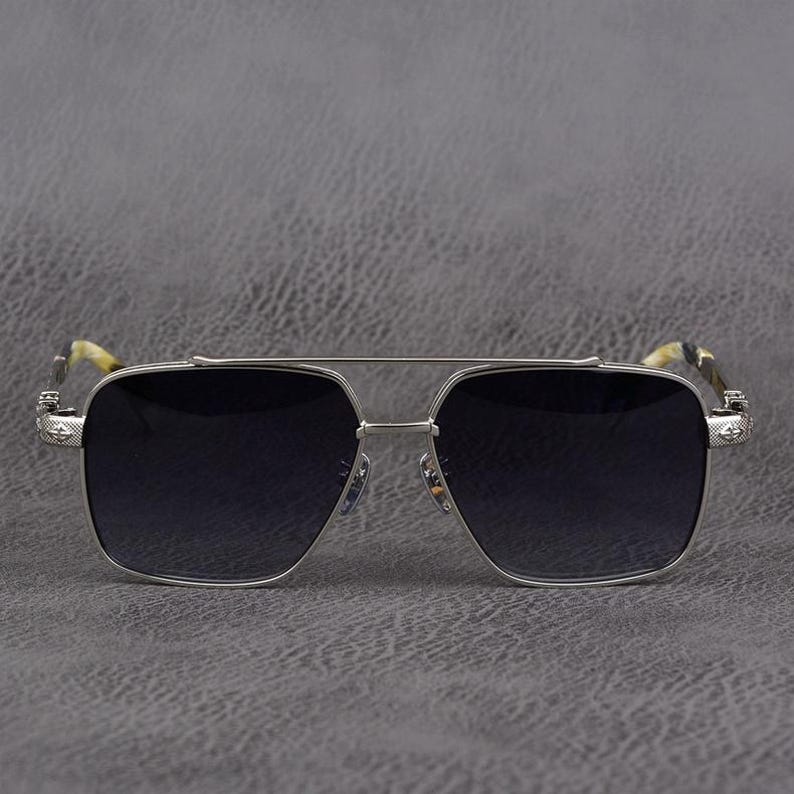 Puede incluir: Gafas de sol con montura plateada y lentes oscuras. Las gafas tienen un doble puente y detalles decorativos en las patillas. Las patillas tienen un patr&oacute;n de camuflaje.