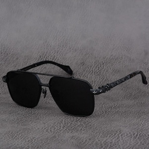 Puede incluir: Gafas de sol aviador negras con doble puente y lentes oscuras. Las monturas son de metal gris oscuro con patillas estampadas. Las gafas de sol est&aacute;n sobre un fondo gris.