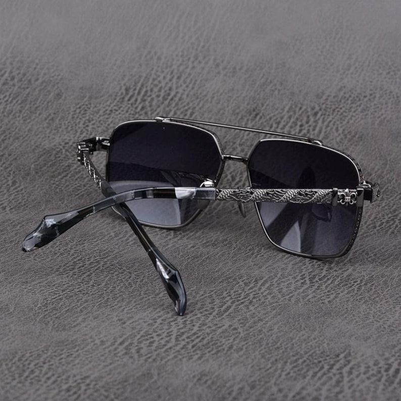 Puede incluir: Gafas de sol grises oscuras con doble puente y lentes cuadradas. Las monturas son de color met&aacute;lico oscuro con detalles decorativos en las patillas. Las lentes son de color gris oscuro.