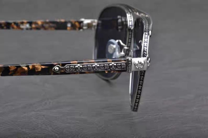 Puede incluir: Primer plano de gafas de sol con montura plateada y lentes oscuras. Las patillas tienen un patr&oacute;n de carey y est&aacute;n adornadas con detalles plateados decorativos. Las bisagras y los detalles de la montura presentan dise&ntilde;os intrincados.