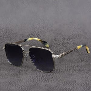 Puede incluir: Gafas de sol con montura plateada y lentes oscuras. Las patillas presentan un dise&ntilde;o estampado y un efecto veteado amarillo y negro. Las gafas tienen doble puente y lentes cuadradas, ofreciendo un look cl&aacute;sico y elegante.