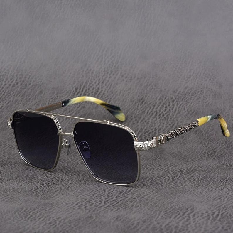 Puede incluir: Gafas de sol con montura plateada y lentes oscuras. Las patillas presentan un dise&ntilde;o estampado y un efecto veteado amarillo y negro. Las gafas tienen doble puente y lentes cuadradas, ofreciendo un look cl&aacute;sico y elegante.